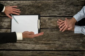 Tisch von oben, zwei Personen, von denen man nur die Hände sieht, sitzen sich gegenüber