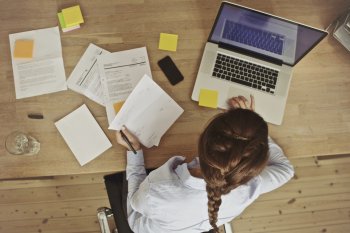 Sicht von oben auf Studentin, die mit Laptop und Unterlagen am Tisch sitzt