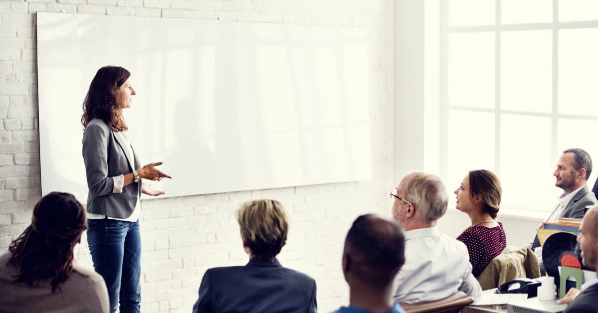 Dozentin steht vorne an Whiteboard, um sie herum sitzen ältere Studenten